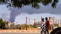 Men walk down a street in Khartoum on June 8, 2023, as smoke rises from behind buildings amid continuing fighting between the army and paramilitary forces. 