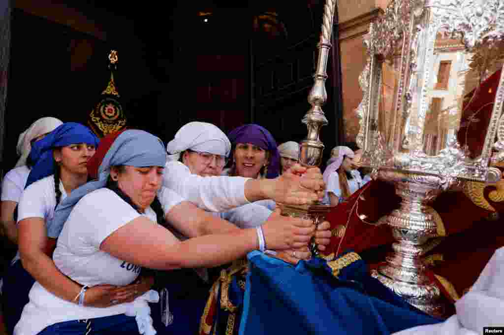 Women &#39;costaleras&#39; acting as &#39;penitents&#39; belonging to Cristo Resucitado y Nuestra Senora de Loreto brotherhood hold a structure in a ramp while others carry a statue of the Virgin Mary on a structure traditionally known as &#39;paso&#39;, as they leave a church during an Easter Sunday procession, the last day of Holy Week, in Ronda, Spain.&nbsp;