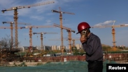 资料照：一名打手机的工人走过北京的一处建筑工地。（2022年4月14日）