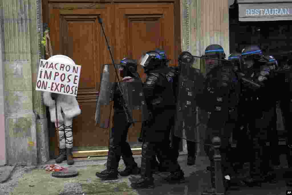 Seorang pengunjuk rasa bersembunyi di balik poster bertuliskan &quot;Macron memaksa, kami meledak&quot; selama demonstrasi menentang rencana tidak populer Presiden Prancis Emmanuel Macron untuk menaikkan usia pensiun, di Paris, Prancis.