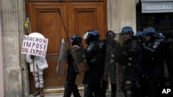 FILE: A protester hides behind a poster reading "Macron impose, we explode" during a demonstration in Paris, France, April 13, 2023. The nation's top court is expected to rule Friday, April 14, on the constitutionality of Macron's upward pension age move. 