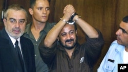 FILE - Marwan Barghouti raises his handcuffed hands in the air on the opening day of his trial at Tel Aviv's District Court on Aug. 14, 2002. 