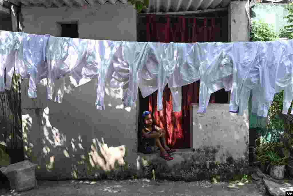 A girl sits next to a line with washed shirts drying at an open-air laundry in New Delhi, India.