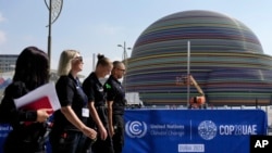 Pessoas caminham junto a um logótipo da Cimeira do Clima da ONU COP28 no Dubai, Emirados Árabes Unidos, 29 de novembro de 2023.