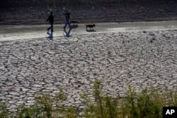 FILE - People walk by cracked earth in an area once under the water of Lake Mead at the Lake Mead National Recreation Area, Jan. 27, 2023, near Boulder City, Nevada.