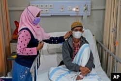 Misnar, right, a street vendor who suffers from pneumonia, sits on his bed as his daughter Siti Nurzanah adjusts his mask at Persahabatan Hospital in Jakarta, Indonesia, on Sept. 22, 2023.
