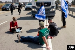 Pengunjuk rasa Israel memblokir jalan menuju truk Yordania yang membawa pasokan bantuan kemanusiaan yang tiba di sisi Israel di perbatasan Kerem Shalom dengan Jalur Gaza di Israel selatan pada 16 April 2024. (Foto: AFP)