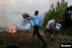 Policajac i vatrogasac bacaju vodu iz kanti na plamen tokom požara u Kaškaišu, Portugal, 25. jula 2023.