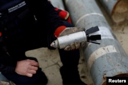 FILE - A Ukrainian military serviceman holds a defused cluster bomb among a display of pieces of Russian army rockets that a Ukrainian munitions expert said did not explode on impact, in Kharkiv region, Ukraine, Oct. 21, 2022.