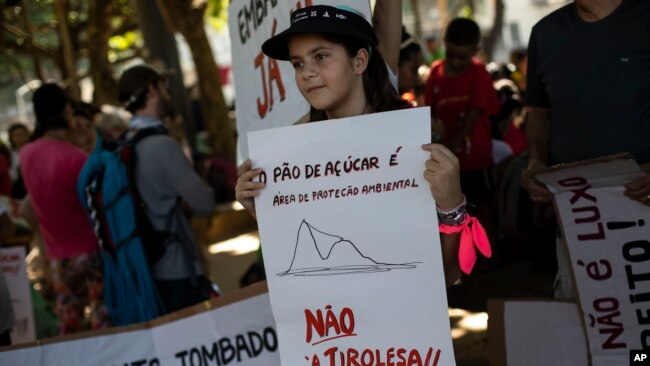 A child holds a sign that reads in Portuguese 'Sugar Loaf Mountain is an environmental protection area. Not the zip line,' during a protest against the installation of a zip line on Sugar Loaf Mountain, in Rio de Janeiro, March 26, 2023.