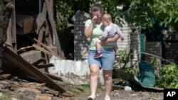 A woman cries as she carries her child, leaving the scene of a Russian rocket attack that ruined her house in Stari Petrivtsi close to Kyiv, Ukraine, June 16, 2023.