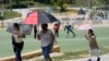 Los visitantes se cubren del calor con sombrillas a medida que aumentan las temperaturas en MacArthur Park, el martes 11 de julio de 2023 en Los Ángeles. (Foto AP/Marcio José Sánchez)