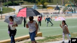 Los visitantes se cubren del calor con sombrillas a medida que aumentan las temperaturas en MacArthur Park, el martes 11 de julio de 2023 en Los Ángeles. (Foto AP/Marcio José Sánchez)