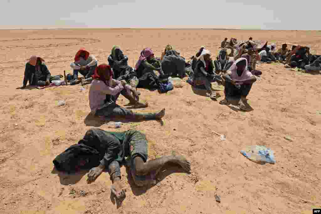Migrants from sub-Saharan African countries who claim to have been abandoned in the desert by Tunisian authorities without water or shelter, sit in an uninhabited area near Libya&#39;s border town of Al-Assah.