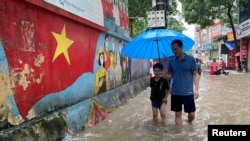A man and a boy walk through a flooded street after heavy rains in Hanoi, Vietnam, Sept. 28, 2023.