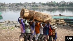 Laborers carry a log of wood from a cargo boat near the Buriganga river in Dhaka, Bangladesh.