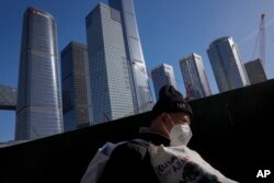 Seorang pekerja migran yang mengenakan masker berjalan melewati derek konstruksi dekat gedung perkantoran di kawasan pusat bisnis di Beijing, 15 Maret 2023. (Foto: Andy Wong/AP Photo)