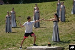 Actress Mary Mina, playing a priestess, hands an olive branch to the first torch bearer, Greek olympic gold medalist Stefanos Douskos, during the final dress rehearsal of the flame lighting ceremony for the Paris Olympics at the Ancient Olympia site, Greece, April 15, 2024.