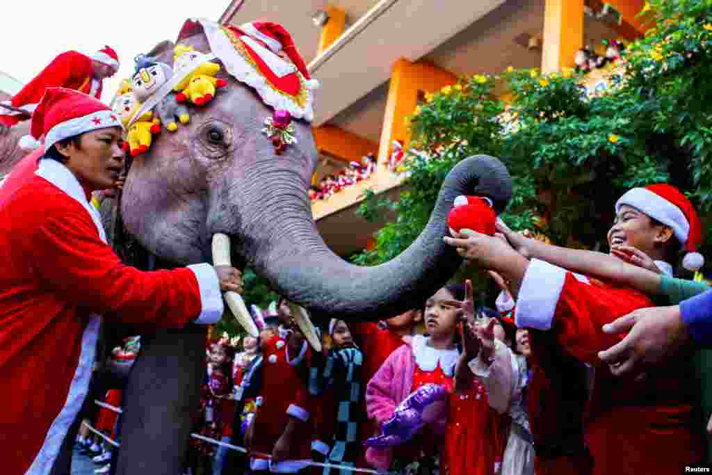 Students wait for gifts from an elephant dressed in a Santa Claus costume ahead of Christmas celebrations at a school, in Ayutthaya, Thailand.