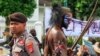Seorang pemuda Papua (kanan) dalam pakaian tradisional, yang wajahnya dicat dengan warna Bendera Bintang Kejora yang dilarang pemerintah, saat demonstrasi menuntut referendum kemerdekaan provinsi Papua di Yogyakarta, 1 Desember 2023. (Foto: DEVI RAHMAN/AFP)