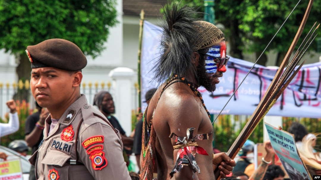 Seorang pemuda Papua (kanan) dalam pakaian tradisional, yang wajahnya dicat dengan warna Bendera Bintang Kejora yang dilarang pemerintah, saat demonstrasi menuntut referendum kemerdekaan provinsi Papua di Yogyakarta, 1 Desember 2023. (Foto: DEVI RAHMAN/AFP)