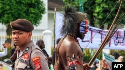ILUSTRASI - Seorang pria berpakaian tradisional Papua dengan wajah dicat warna Bendera Bintang Kejora yang dilarang Indonesia, berdiri di samping seorang polisi selama demonstrasi menuntut referendum kemerdekaan provinsi Papua di Yogyakarta, 1 Desember 2023. (DEVI RAHMAN / AFP) 