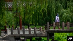 FILE - A woman walks across a bridge at a public park in Beijing, June 7, 2022. 