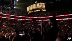 FILE - Wrestling fans, under a Wrestlemania sign, watch a WWE Monday Night RAW event, March 6, 2023, in Boston.