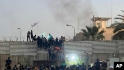Protesters scale a wall at the Swedish Embassy in Baghdad Thursday, July 20, 2023. Protesters angered by the planned burning of a copy of the Quran stormed the embassy early Thursday, breaking into the compound and lighting a small fire.