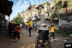 Seorang pria Palestina duduk di kursi rodanya ketika orang-orang berkeliaran di sepanjang jalan yang sebagian hancur menyusul pengeboman Israeldi Khan Yunis dan wilayah lain di Jalur Gaza pada 27 Oktober 2023. (Foto: AFP)