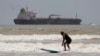 An oil taker heads out to open water as a surfer takes advantage of waves ahead of Hurricane Beryl's arrival in Port Aransas, Texas, July 6, 2024. 