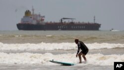 An oil taker heads out to open water as a surfer takes advantage of waves ahead of Hurricane Beryl's arrival in Port Aransas, Texas, July 6, 2024. 