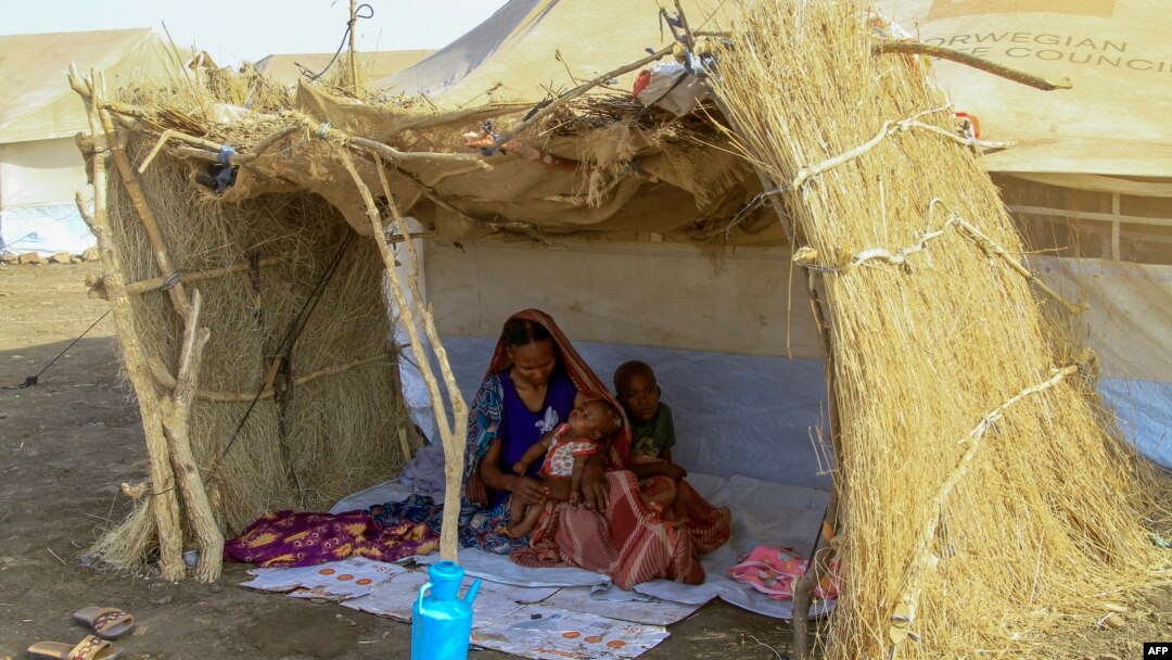 FILE - A displaced woman and her children sit in the shade of a straw hut at a camp in southern Gadaref state, for people who fled Khartoum and Jazira states in war-torn Sudan, March 20, 2024.