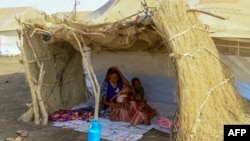 FILE - A displaced woman and her children sit in the shade of a straw hut at a camp in southern Gadaref state, for people who fled Khartoum and Jazira states in war-torn Sudan, March 20, 2024.
