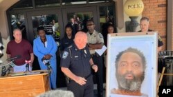 En esta foto tuiteada por Steve Gehlbach de WSB-TV, el jefe de Policía de Hampton, James Turner, en el centro, junto a una foto montada del sospechoso Andre Longmore durante una conferencia de prensa en Hampton, Georgia, el sábado 15 de julio de 2023.