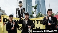 Peserta yang mengenakan masker wajah tiga calon presiden Anies Baswedan, Prabowo Subianto, dan Ganjar Pranowo berjalan di depan boneka raksasa bergambar Pinokio saat demonstrasi di Jakarta, 7 Februari 2024. (Foto : AFP/Yasuyoshi CHIBA)