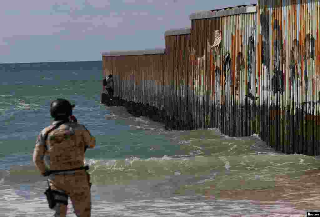 A member of the Mexican National Guard stands guard as a man tries to climb the wall at Playas de Tijuana, in Tijuana, Mexico, Feb. 14, 2024.