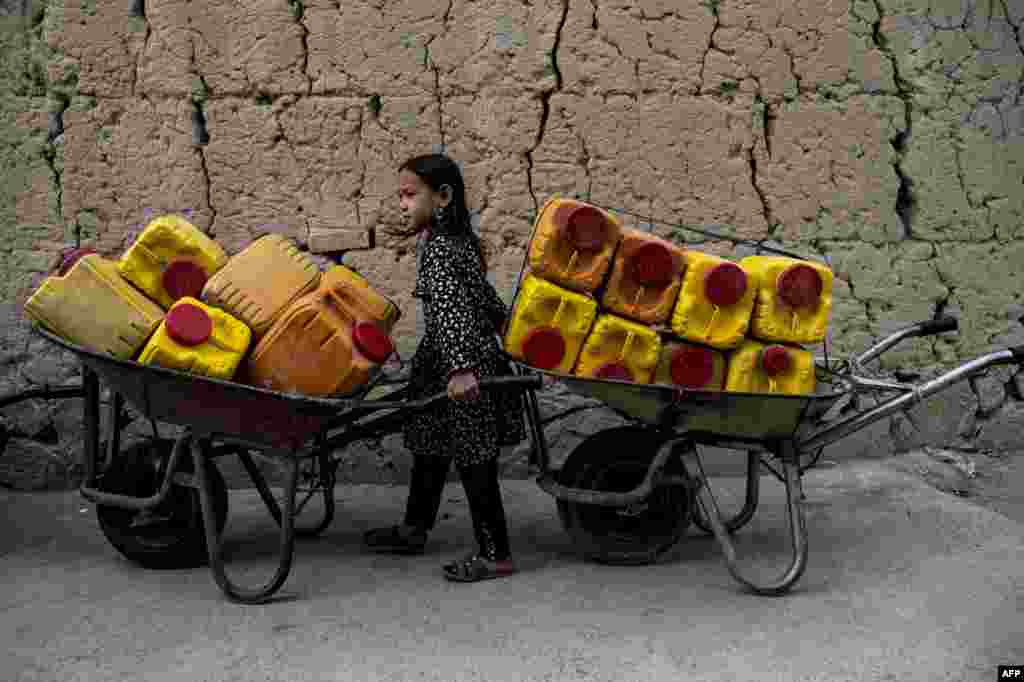 A girl pushes a wheelbarrow loaded with canisters to fill with drinking water supplied by a private group at Regretion area in Dasht-e-Barchi in Kabul, Afghanistan.