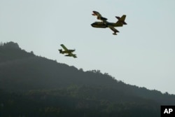 An Air Tractor, left, and a Canadair, firefighting airplanes, pass each other while working on a wildfire burning near houses in Alcabideche, outside Lisbon, Tuesday, July 25, 2023.