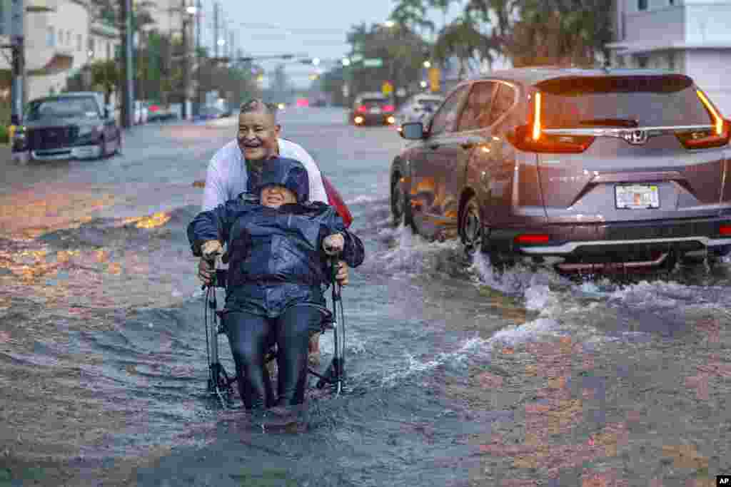 Víctor Corone, de 66 años, empuja a su esposa María Díaz, de 64 años, en una silla de ruedas a través de más de un pie de agua de inundación en la calle 84 en Miami Beach, Florida.