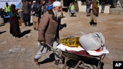 FILE - An Afghan man carries supplies in a wheelbarrow during a distribution of aid in Kabul, Feb. 16, 2022. U.S. officials, in recent talks with Taliban leaders, noted data indicating falling inflation and growing trade in Afghanistan in 2023.