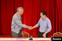 Perdana Menteri Singapura, Lee Hsien Loong, berjabat tangan dengan Menteri Keuangan Lawrence Wong selama konferensi pers di Istana, Singapura pada 16 April 2022. (SPH Media/The Straits Times/Lim Yaohui via REUTERS)