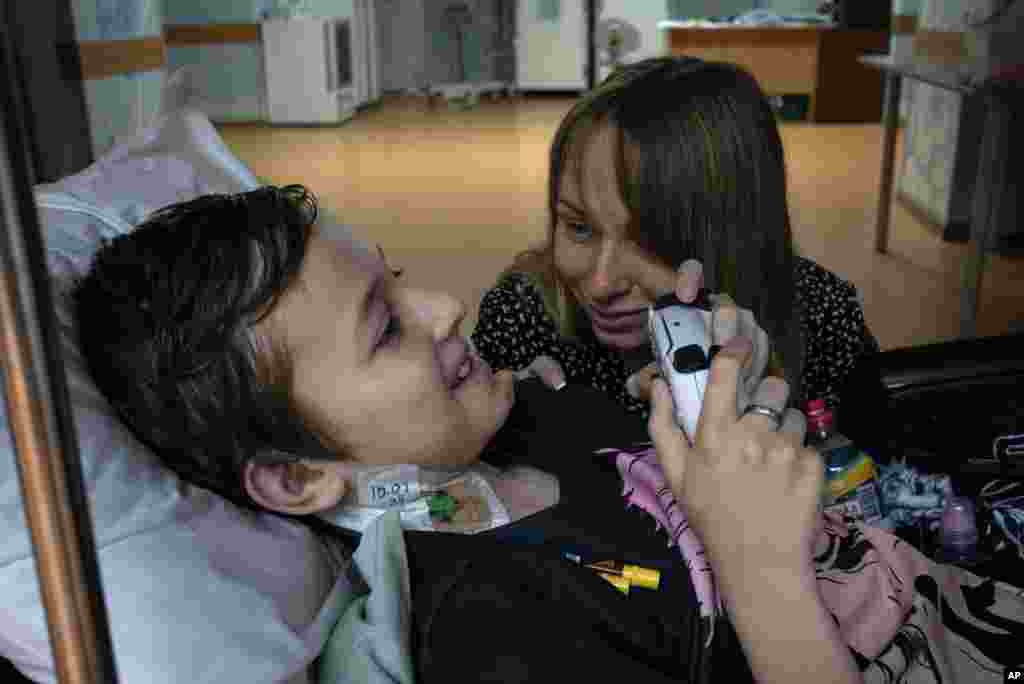 Yuliia Vasylenko sonríe con su hijo Denys, de 11 años, mientras juega en una consola de videojuegos en el Instituto Nacional del Cáncer en Kiev, Ucrania, el 10 de julio de 2024. (Foto AP/Alex Babenko)