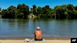 Seorang pria tampak berusaha mendinginkan badannya di pinggir danau di Sacramento, California, pada 2 Juli 2024. (Foto: AP/Terry Chea)