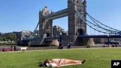 FILE - A woman sunbathes on the grass at Potters Field near Tower Bridge on a hot day in London, June 25, 2023.