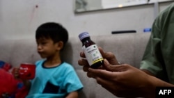 FILE - Riski Agri (R) displays a bottle of cough syrup that was consumed by his son Farrazka which caused him kidney problems, at their house in Jakarta, Indonesia, Feb. 11, 2023.