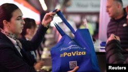 Seorang staf maskapai penerbangan memberikan tas jinjing dengan tanda bertuliskan "#TanpaVisa" saat warga Kosovo mulai melakukan perjalanan ke wilayah Schengen di Eropa, di bandara Pristina 1 Januari 2024. 