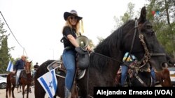 Una joven sostiene un megáfono mientras participa con con su caballo en la cabalgata por el regreso a casa del joven Idam Shtivi, el 5 de diciembre de 2023.