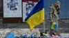 কিয়েভের স্বাধীনতা চত্বরে নিহত সেনাদের প্রতি সম্মান জানানোর জন্য নির্মিত অস্থায়ী স্মৃতিসৌধে ইউক্রেনীয় পতাকার সামনে দাঁড়িয়ে শোক প্রকাশ করছেন এক সেনাসদস্য (১০ নভেম্বর, ২০২৩) 