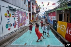 Anak-anak bermain sepak bola di dekat mural bertema Piala Dunia FIFA Qatar di Desa Pambusuang, Sulawesi Barat, Minggu, 20 November 2022. (Foto: AP)